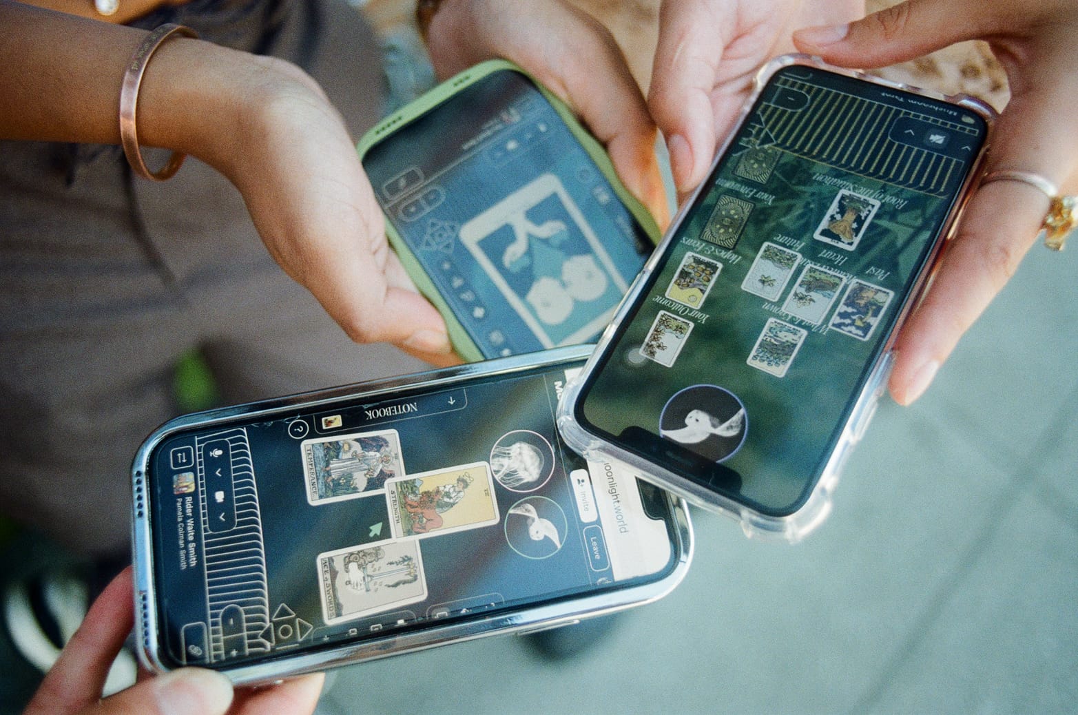 Three friends each holding a phone, with each phone depicting a different tarot deck